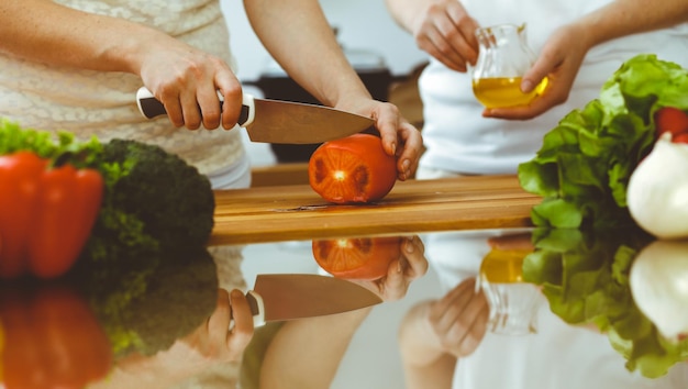 Close-up van menselijke handen koken in de keuken Moeder en dochter of twee vriendinnen die groenten snijden voor verse salade Vriendschap familiediner en lifestyle concepten