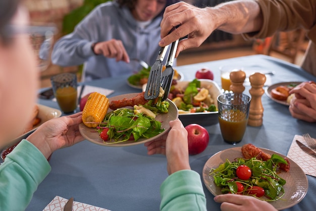 Close-up van mensen die groentesalade op bord zetten tijdens het diner aan tafel