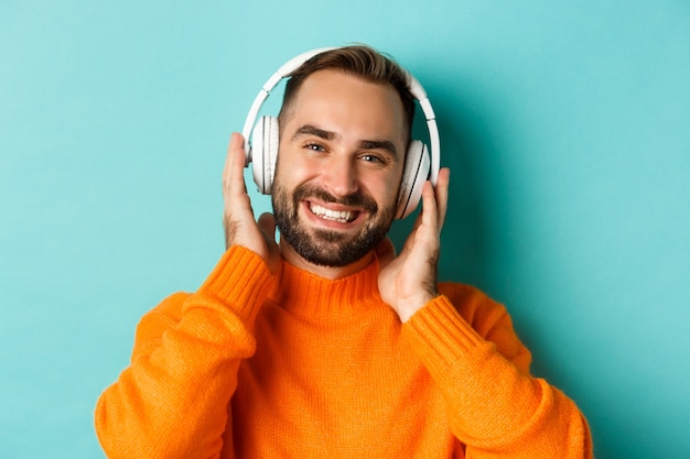 Close-up van moderne man luisteren muziek in koptelefoon, permanent in oranje trui