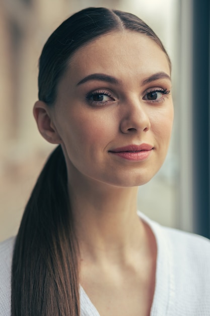 Foto close-up van mooie jonge langharige vrouw met natuurlijke make-up die naar de camera kijkt en zorgvuldig glimlacht