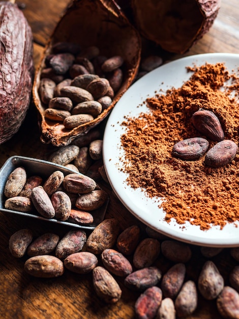 Foto close-up van natuurlijk cacaopoeder met bruine cacaobonen en droge cacaobollen op een vintage houten tafel