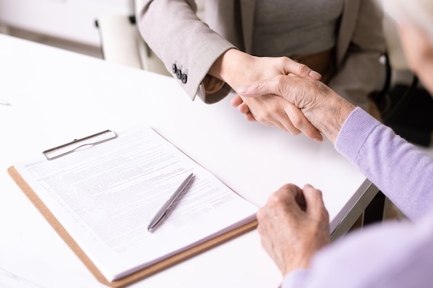 Close-up van onherkenbaar maatschappelijk werkerhandshaking met oudere dame na ondertekening van document