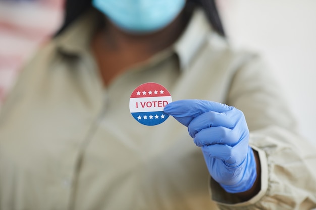 Close-up van onherkenbare afro-amerikaanse vrouw met i voted sticker terwijl staande op stembureau op post-pandemie verkiezingsdag, kopie ruimte