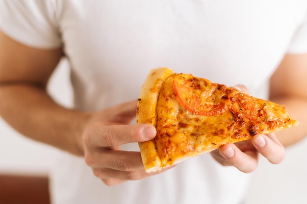 Close-up van onherkenbare man met witte kleren die een stuk smakelijke pizza in handen houdt op een witte geïsoleerde achtergrond