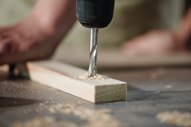 Close-up van onherkenbare timmerman die houten plank boort om gaten op de werkplek te maken