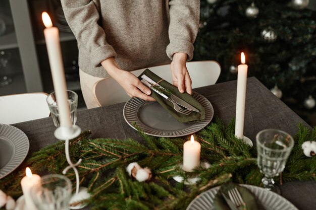 Close-up van onherkenbare vrouw die eettafel opzet voor kerstmis versierd met dennentakken en...