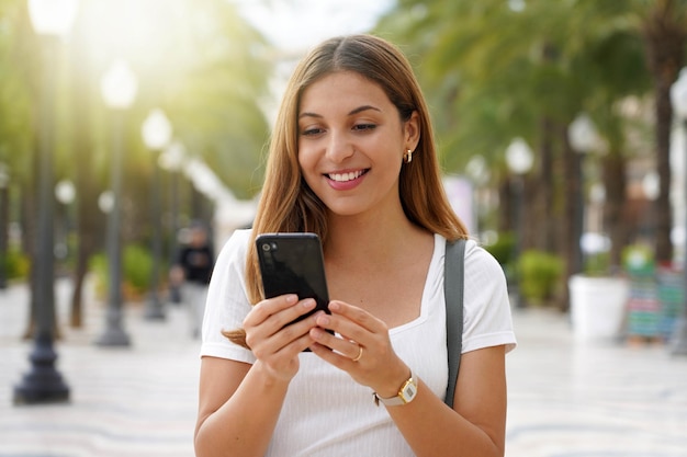 Close up van opgewonden jonge vrouw die naar haar smartphone kijkt wanneer ze op straat loopt Millennial meisje met mobiele app buitenshuis Tiener levensstijl technologie concept