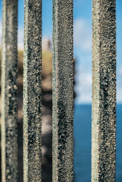 Close-up van oude roestige metalen omheining op rotsachtige klif over eindeloze blauwe zee op zonnige dag