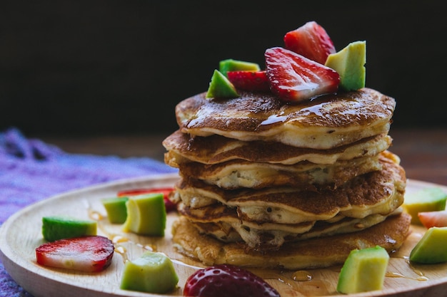 Close-up van pannenkoeken met fruit geserveerd op een bord op tafel tegen een zwarte achtergrond