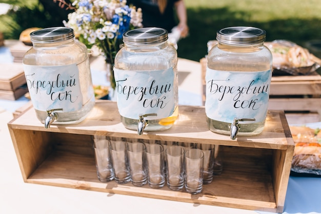 Close-up van picknickfeest in parkdranktafel met grote kruik en glazen flessen gevuld met ijskoude roze limonade en verse citroenen, roze wervelend stro, lepels en teken op roze gingangtafelkleed