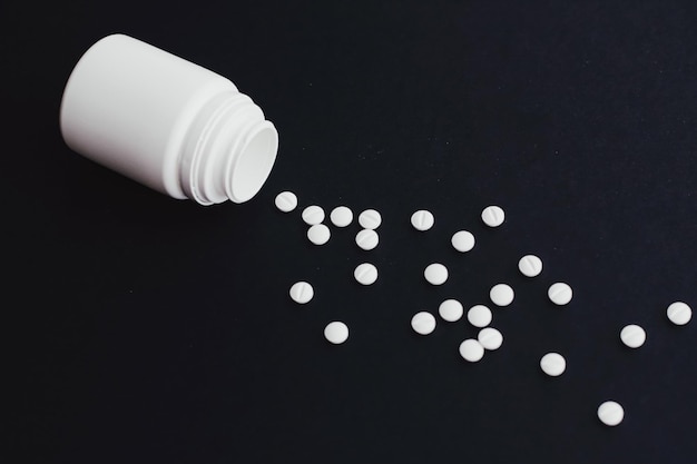 Foto close-up van pillen die uit de fles stromen tegen een zwarte achtergrond