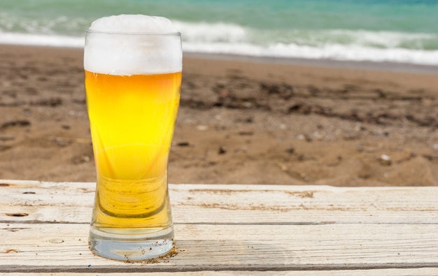 Close-up van pint bier of pils door zandstrand met de zee op de achtergrond.