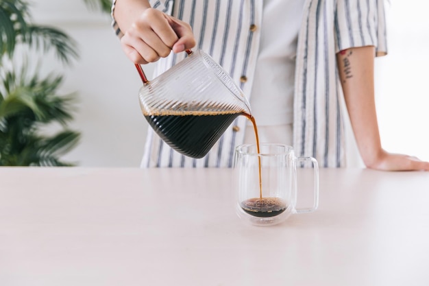 Close-up van professionele barista-hand die vers gezette koffie in een glazen mok giet. Koffie alternatieve methode bereiden