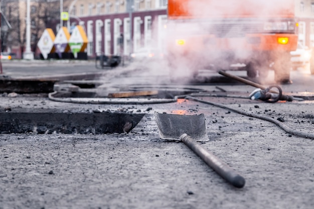 Close-up van professionele hulpmiddelen voor asfaltreparatie, wegkuil, schop, bitumen tegen stadsachtergrond.