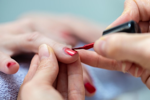 Close-up van professionele manicure die glanzende roze nagellak toepast om nagels perfect te vormen in een cosmetische salon