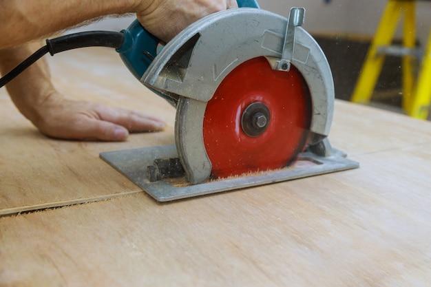 Close-up van professionele schrijnwerker die met elektrische cirkelzaag bij houtbewerking voor het snijden van houten triplex werken