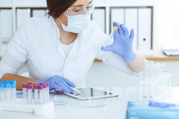 Close-up van professionele vrouwelijke wetenschapper in beschermende brillen die experimenteren met reagentia of bloedonderzoek in het laboratorium. Geneeskunde, biotechnologie en onderzoeksconcept.
