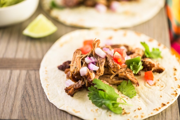 Close up van pulled pork carnitas met pico de gallo op een bloemtortilla.