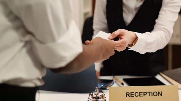 Close-up van receptioniste die de kaartsleutel overhandigt aan elegante Afro-Amerikaanse toerist tijdens het inchecken. Zakenreizende gast die klaar is om te genieten van een hotelverblijf nadat hij toegang tot de kamer heeft gekregen