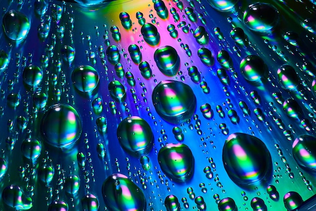Close-up van regendruppels met blauw, paars en groen op reflecterende metalen achtergrond