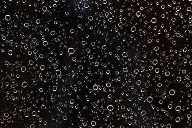 Close-up van regenwaterdruppels achter glas 's avonds. Het ziet eruit als bubbels in zwarte vloeistof. Abstracte natte achtergrond.
