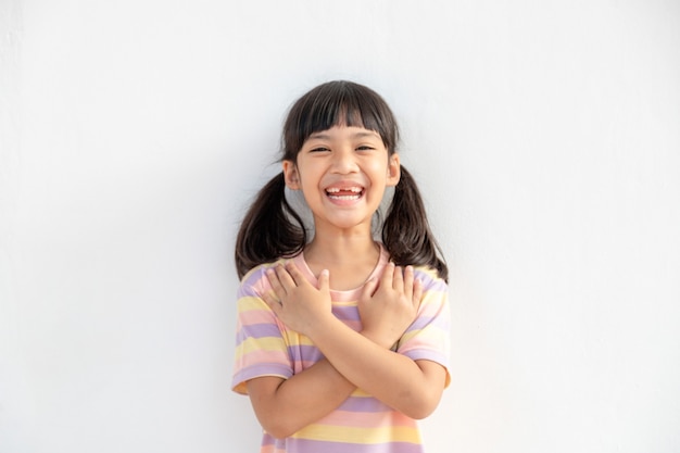 Close up van schattig gelukkig klein meisje geïsoleerd op een witte achtergrond hand in hand op hart borst voel dankbaar, glimlachend klein kind met gesloten ogen bidden dank god hoge krachten, geloof concept