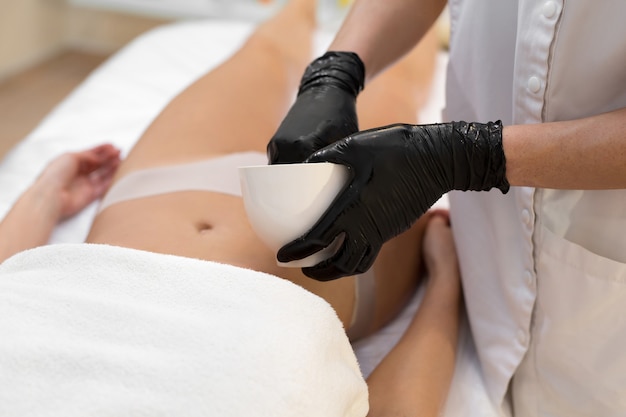 Close-up van schoonheidsspecialist die anticellulitis massage en peeling van de buik met zout aan een jonge vrouw in een kuuroord doet. Huid- en lichaamsverzorging concept.