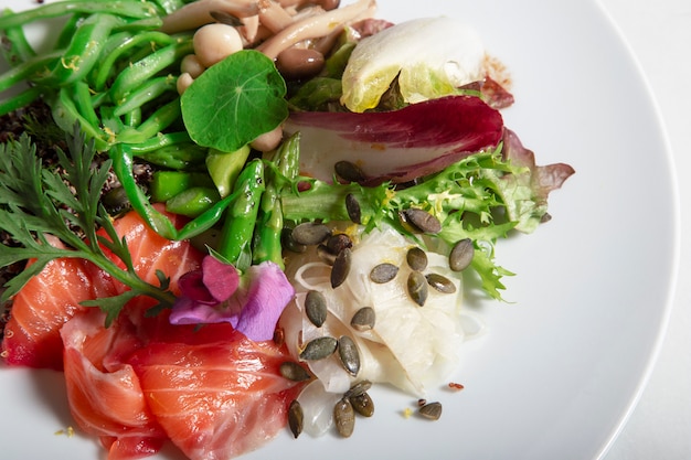 Close-up van schotel van gemarineerde zalm in bieten en dille. Perona sperziebonen, gepekelde venkel, groene asperges, gemarineerde champignons en pompoenpitten. Geïsoleerde afbeelding