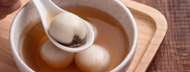 Close up van sesam grote tangyuan (tang yuan, kleverige rijst knoedel ballen) met zoete siroop soep in een kom op houten tafel achtergrond voor winterzonnewende festival voedsel.