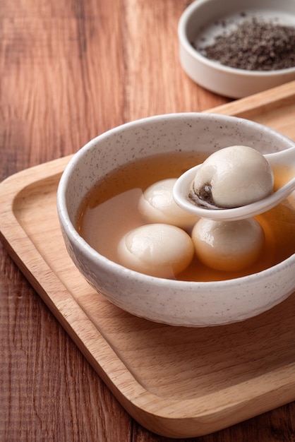 Close up van sesam grote tangyuan (tang yuan, kleverige rijst knoedel ballen) met zoete siroop soep in een kom op houten tafel achtergrond voor winterzonnewende festival voedsel.