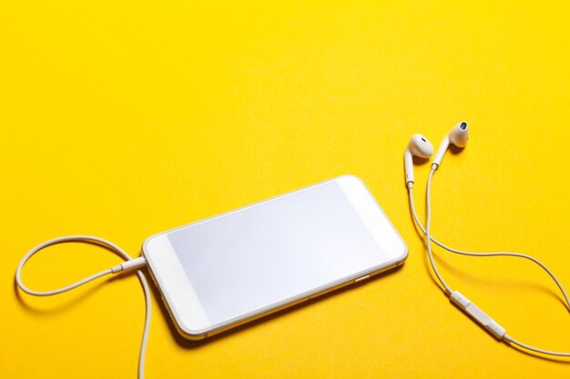 Close-up van slimme telefoon met koptelefoon op een gele achtergrond Bovenaanzicht Luister naar muziek