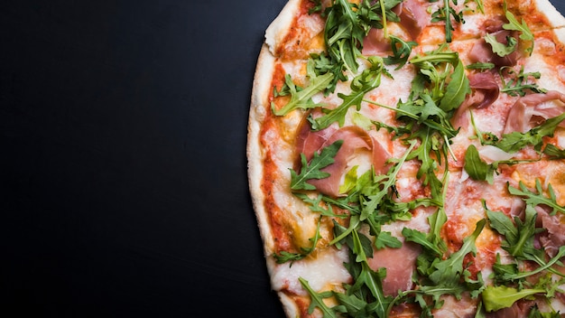 Foto close-up van spek en rucola pizza over zwart oppervlak