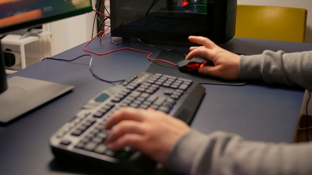 Close-up van spelershanden die RGB-toetsenbord gebruiken in de thuisstudio van gaming. Digitale gamer die 's avonds laat in de woonkamer professionele apparatuur gebruikt voor de wedstrijd van de eerste shooter-videogamepersoon