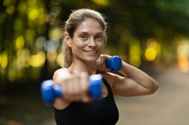 Close-up van sterke atletische vrouw die buiten met halters traint