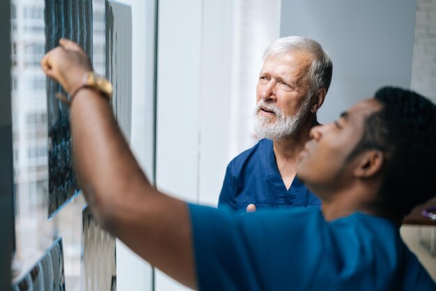 Close-up van team multi-etnische artsen die samen de geschiedenis van de ziekte van de patiënt bespreken met behulp van MRI-scan tijdens een medische bijeenkomst die bij het raam staat. Concept van geneeskunde en gezondheidszorg.