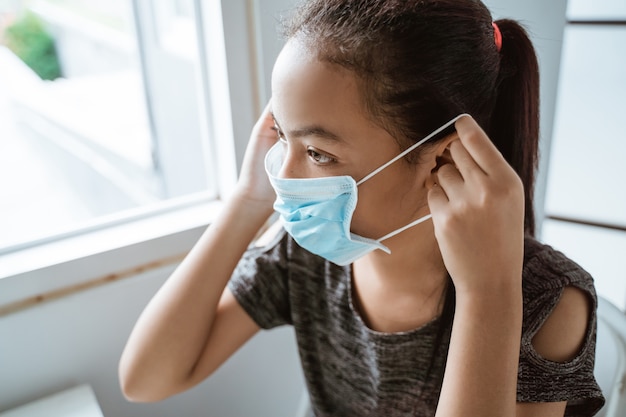 Close-up van tiener meisje draagt ?? een masker zittend bij het raam