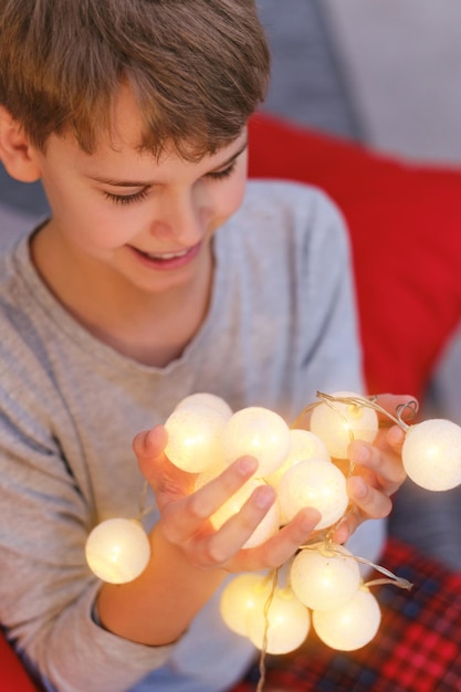 Close-up van tienerjongen met verlichte kerstverlichting thuis