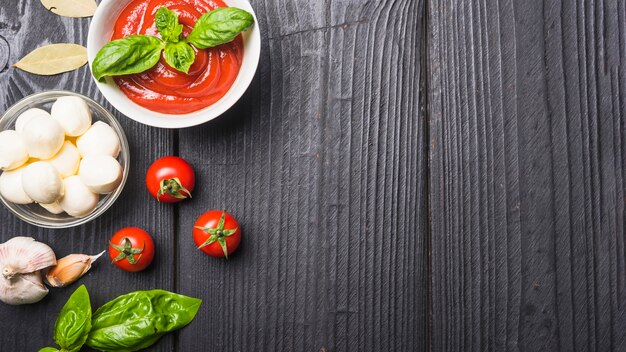 Close-up van tomatensaus met mozarella; pasta; knoflook een basilicum op houten plank