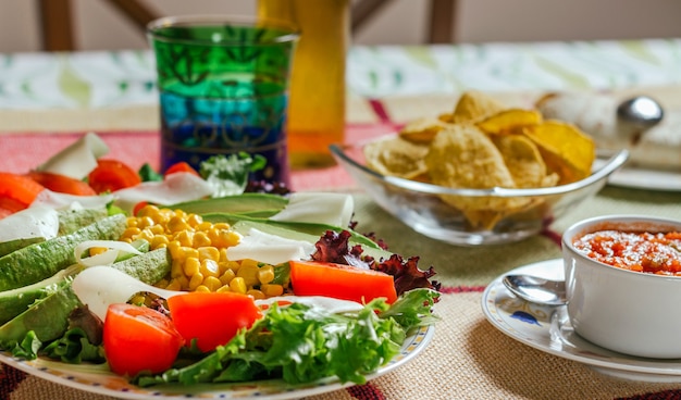 Close-up van traditioneel Mexicaans eten in een tafel, met een bord verse salade, nacho's en een kom pikante saus