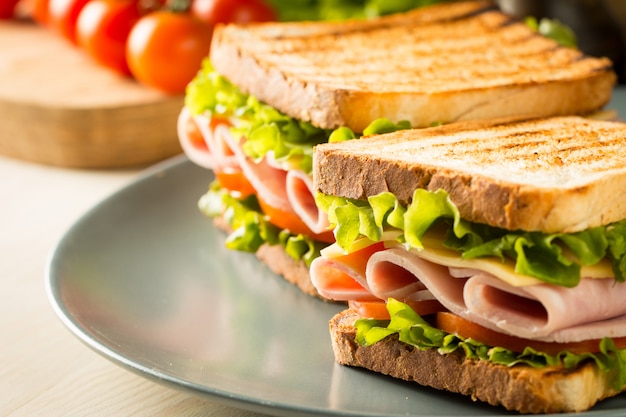 Close-up van twee broodjes met spek, salami, prosciutto en verse groenten op rustieke houten snijplank. Club sandwich concept.