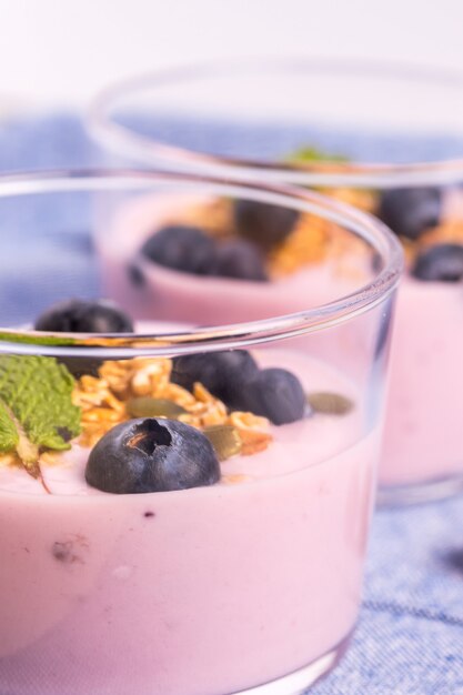 Foto close-up van twee glazen aardbeienyoghurt met bosbessen en ontbijtgranen op een blauw tafelkleed