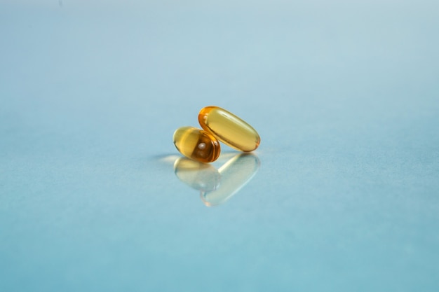 Close-up van twee omega-3 capsules op blauwe achtergrond met reflectie. Gezondheidszorgconcept.