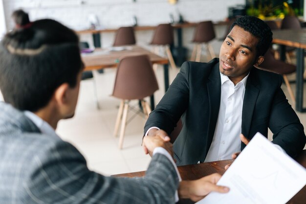 Close-up van twee tevreden multiraciale zakenlieden die elkaar de hand schudden na succesvolle onderhandelingen bij het sluiten van een verzegeldeal
