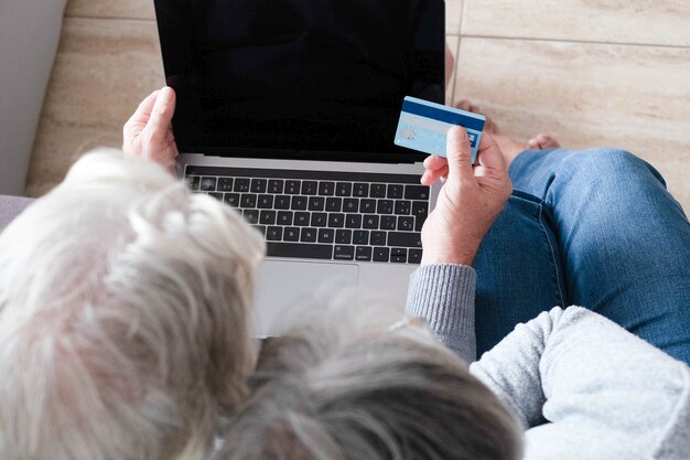 Close-up van twee volwassen mensen die een creditcard gebruiken om samen thuis op de bank online te winkelen - senioren die geld uitgeven