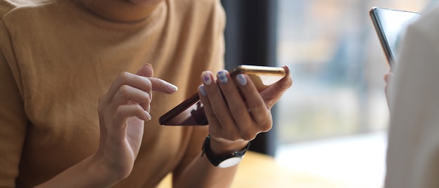 Close-up van twee vrouwtjes met behulp van smartphone terwijl ze tegenover elkaar zitten