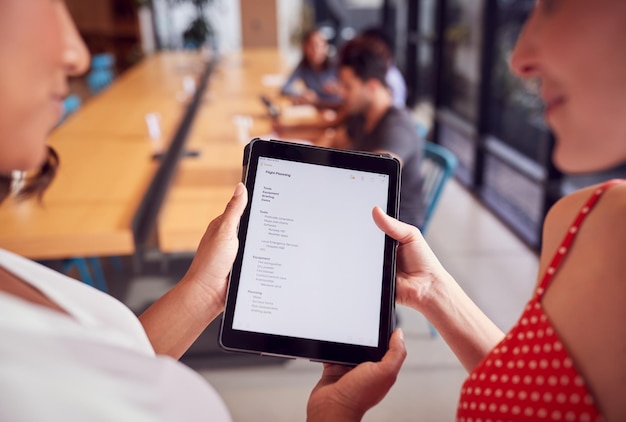 Close-up van twee zakenvrouwen die naar digitale tablet kijken in een gedeelde kantoorwerkruimte