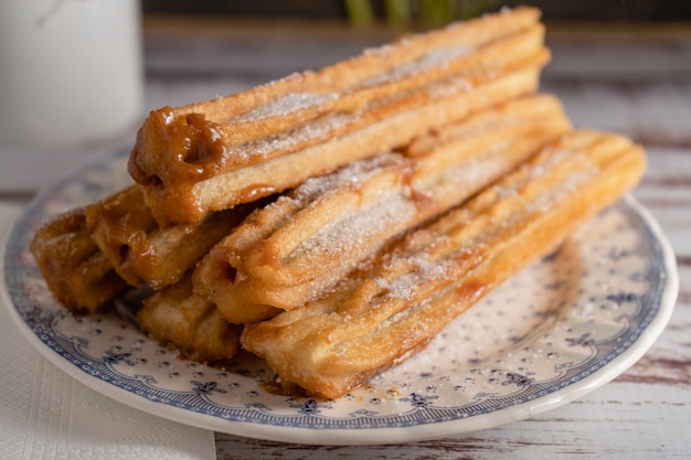 Close-up van typische Spaanse churros gevuld met dulce de leche in een vintage bord op oude planken.