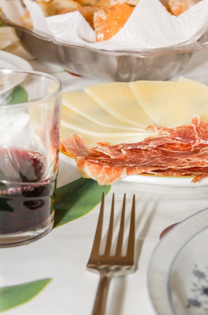 Close-up van typische spaanse tapa, met plakjes serranoham en manchego-kaas geserveerd in een bord, vergezeld van een glas rode Rioja-wijn