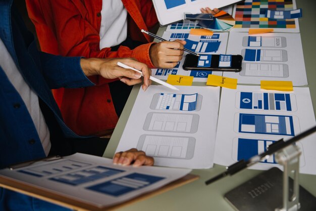 Close-up van ux-ontwikkelaar en ui-ontwerper brainstormen over wireframe-ontwerp van de mobiele app-interface op tafel met klant breif en kleurcode op modern kantoor Creatief bureau voor digitale ontwikkeling