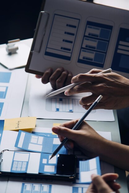 Close-up van ux-ontwikkelaar en ui-ontwerper brainstormen over wireframe-ontwerp van de mobiele app-interface op tafel met klant breif en kleurcode op modern kantoor Creatief bureau voor digitale ontwikkeling